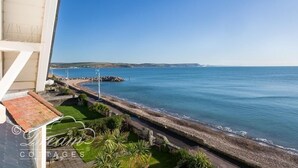 A coastal property with a view of the sea, a stone wall, and a grassy area with a flagpole. - Dream View (Weymouth)