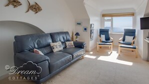 A modern loft-style living room with a dark leather sofa, two blue armchairs, and a large window offering a city view. - Dream View (Weymouth)