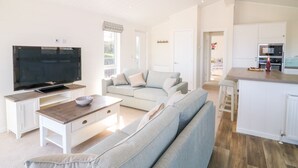 Ein modernes Wohnzimmer mit Flachbildfernseher, einer Couch, einem Couchtisch und einer Küchenzeile mit Mikrowelle und Kühlschrank.