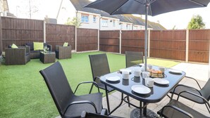 Eine Terrasse im Freien mit einem Tisch für vier Personen, umgeben von Stühlen und einem großen Sonnenschirm, der Schatten spendet.