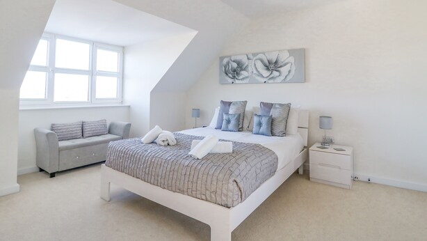 Ein modernes Schlafzimmer mit einem großen Bett, einem grauen Sofa, einem kleinen Tisch und einem Bild an der Wand.