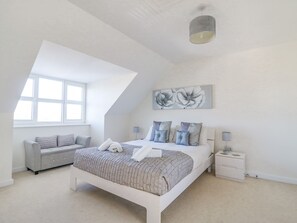 A modern bedroom with a large bed, a grey sofa, a small table, and a painting on the wall. - The Ferns (Weymouth)