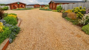 A gravel driveway leading to a row of log cabins with a wooden fence and landscaped gardens.