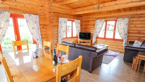 A wooden cabin interior with a dining table, chairs, a sofa, a TV, and a fireplace.
