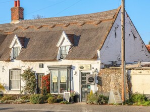 Un bâtiment traditionnel avec un toit de chaume, une enseigne indiquant « Alfredo Tea Rooms », proposant des thés, des scones et des gâteaux, ainsi qu’un petit jardin fleuri.