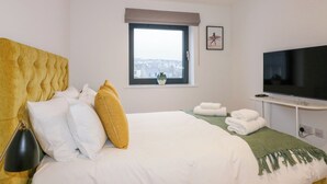 A hotel room with a large bed, a television, a window with a view, and a small table with towels. - Onshore 7 (Newquay)