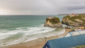A coastal view with a beach, rocky cliffs, and houses on the cliffs. - Onshore 7 (Newquay)