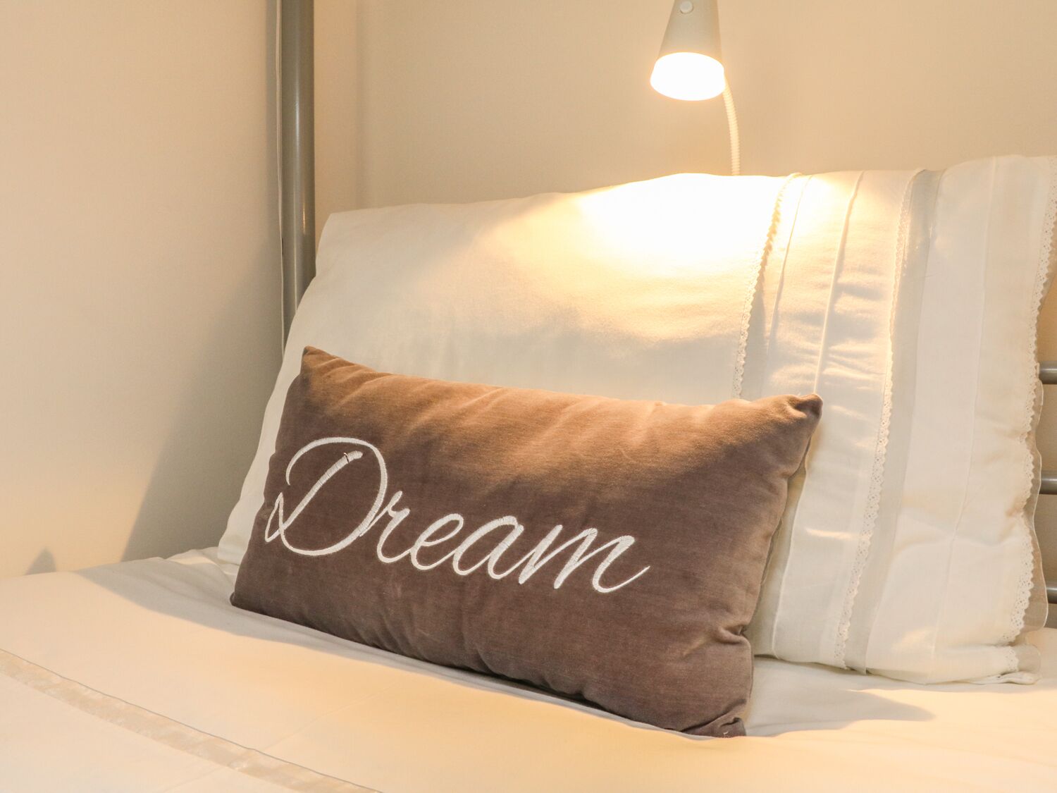A bed with a pillow that has the word "Dream" written on it.