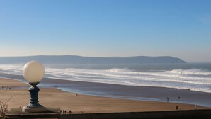 A beach with a spherical object on a pedestal, waves crashing onto the shore, and a clear sky. - Hartland View (Woolacombe)