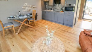 Une cuisine moderne avec des meubles gris, une table à manger en bois et un mur en pierre.