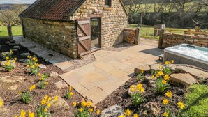 Une charmante maison en pierre avec une porte en bois, un jacuzzi et un jardin où poussent des jonquilles.