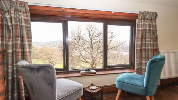 A room with a large window, two chairs, a small table, and plaid curtains. - Cymryd Uchaf (Conwy)