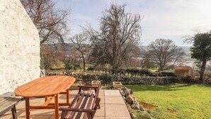 An outdoor patio with a wooden table and benches, a stone wall, and a view of a rural landscape with trees and hills. - Cymryd Uchaf (Conwy)