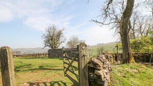 Paisaje rural con un muro de piedra, un portón de madera y un edificio de piedra al fondo.