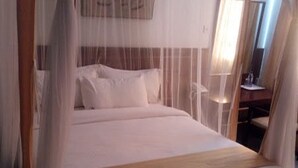 A bed with a canopy, a headboard, and a bedside table with a lamp. - Garden Hotel (Machakos)