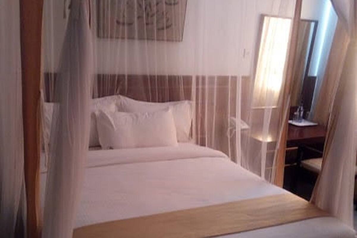 Una cama con dosel, cabecera y mesita de noche con lámpara.