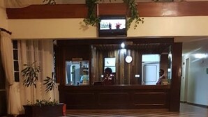 A lobby with a wooden floor, a reception desk, and a television screen. - Garden Hotel (Machakos)