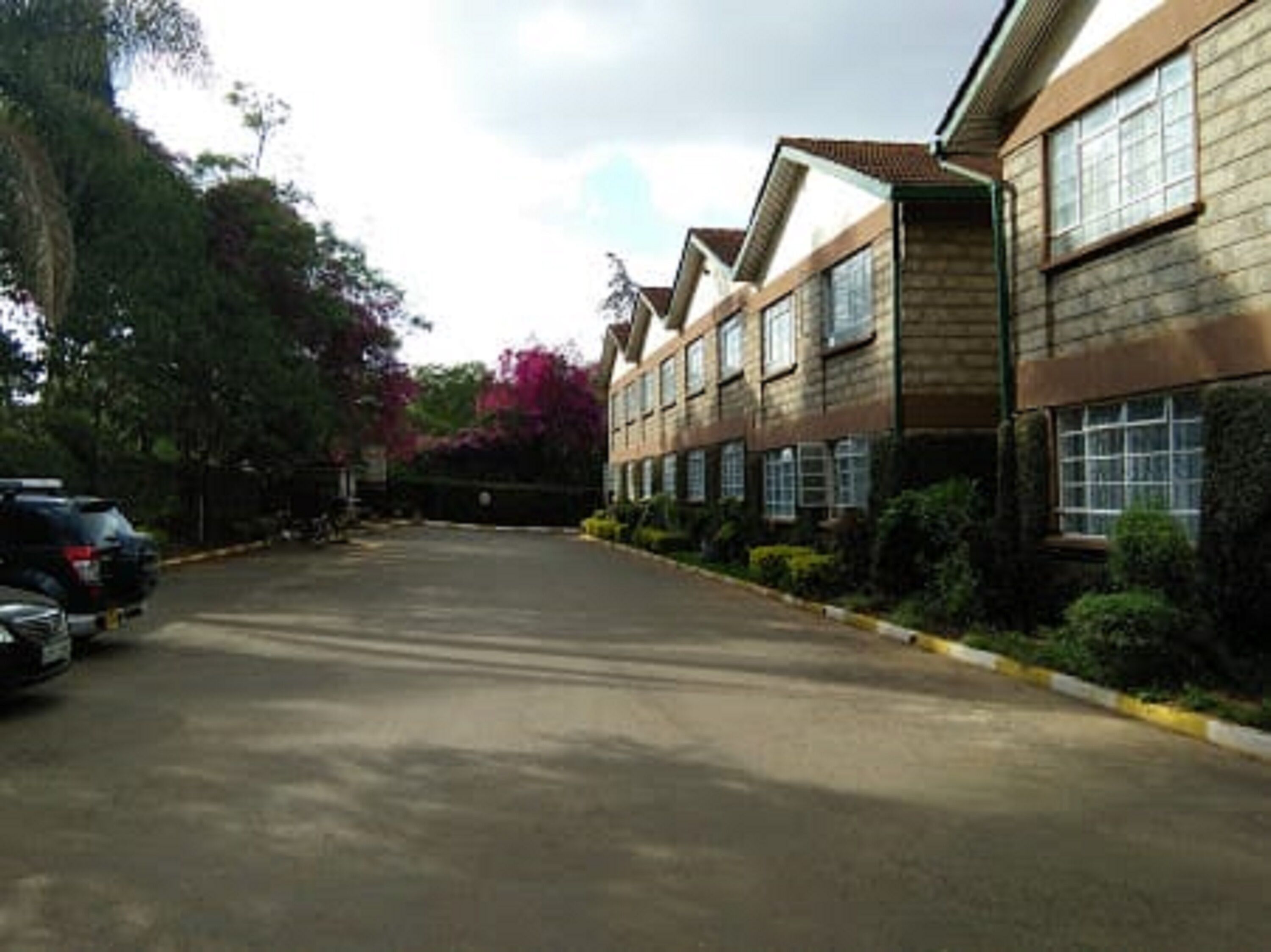 A parking lot with a row of buildings, trees, and parked cars.