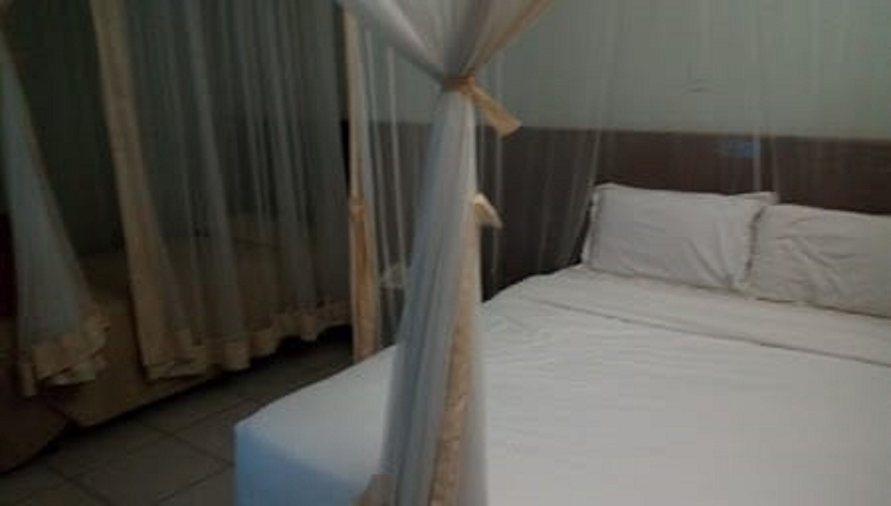 Una cama con sábanas blancas, cabecera de madera y mosquitero.