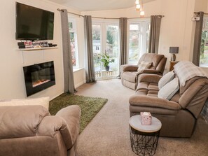 A living room with a flat-screen TV, a fireplace, two sofas, a coffee table, and a view of the outdoors. - The Wee Lodge (Dollar)
