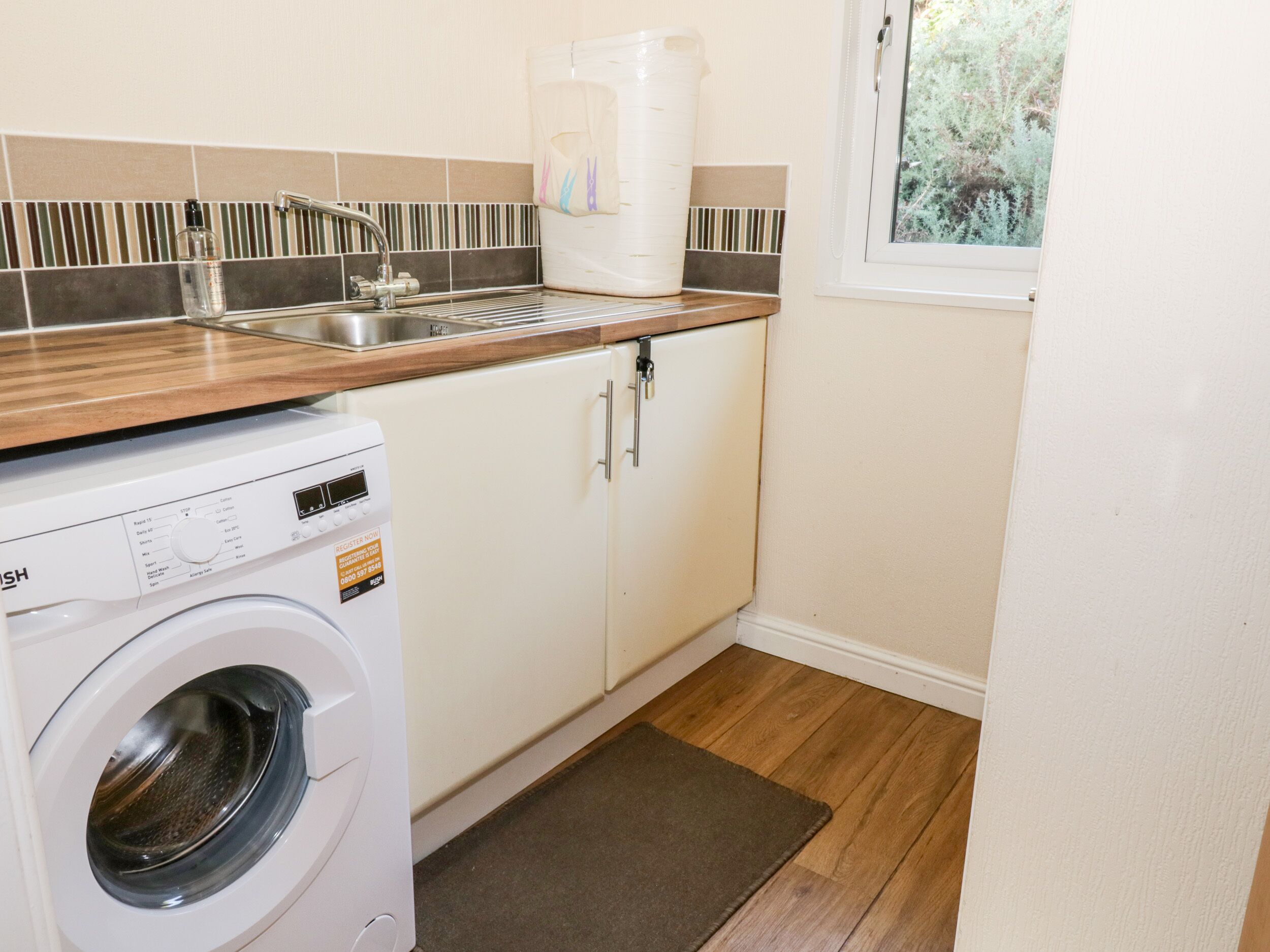A compact kitchen with a washing machine, a sink, and a window with a view of greenery.