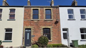 A row of terraced houses with a brick facade, a black door labeled 'Quay Cottage', and a satellite dish on the roof. - Quay Cottage (Weymouth)