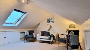 A cozy attic bedroom with a skylight, a white sofa, a chair, and a lamp. - Quay Cottage (Weymouth)