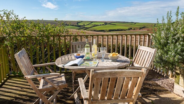 Eine Holzterrasse mit einem runden Tisch und Stühlen, mit Blick auf eine schöne Landschaft.