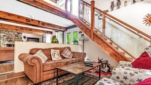 Un vaste espace de vie agrémenté d’un escalier en bois, d’un canapé en cuir, d’un tapis à motifs et de divers objets décoratifs.