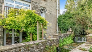 Un mur de pierres, un petit ruisseau, une végétation luxuriante et une treille en bois.
