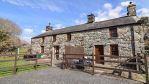 A stone building with multiple windows and doors, a gravel driveway, and a wooden fence. - Cwm Yr Afon Mawr (Llanbedr)