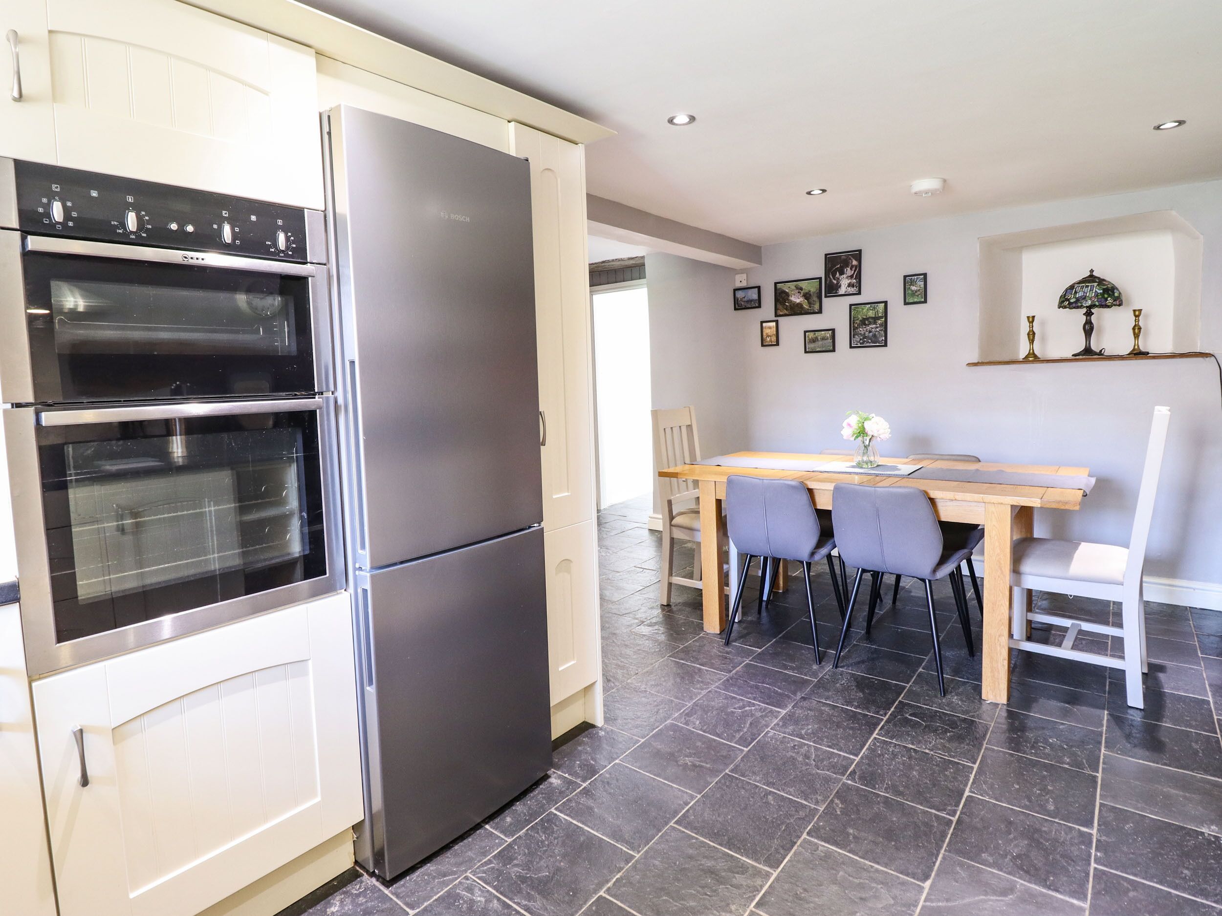 Een moderne keuken met een ingebouwde oven en een grote koelkast. Er staat een eettafel met stoelen en een vaas met bloemen.