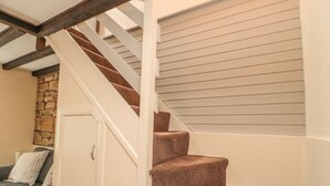 Una escalera con peldaños alfombrados y vigas de madera que conduce a una habitación con pared de piedra y un sofá gris.