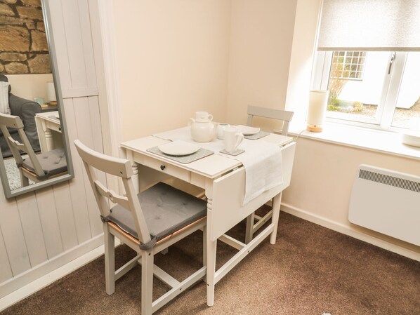 A white dining table with chairs, a mirror, and a window with a view. - Wren Cottage (Morpeth)