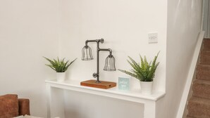 A white wall with a shelf holding three potted plants and a black metal lamp. - Lovatt House Apartment Tynemouth (North Shields)