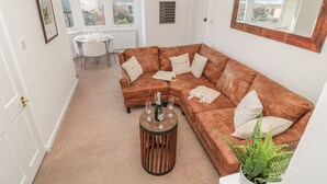 A living room with a brown sectional sofa, a round coffee table, and a potted fern. - Lovatt House Apartment Tynemouth (North Shields)