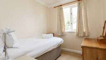 A bedroom with a bed, bedside table, lamp, wooden dresser, and a window with curtains.