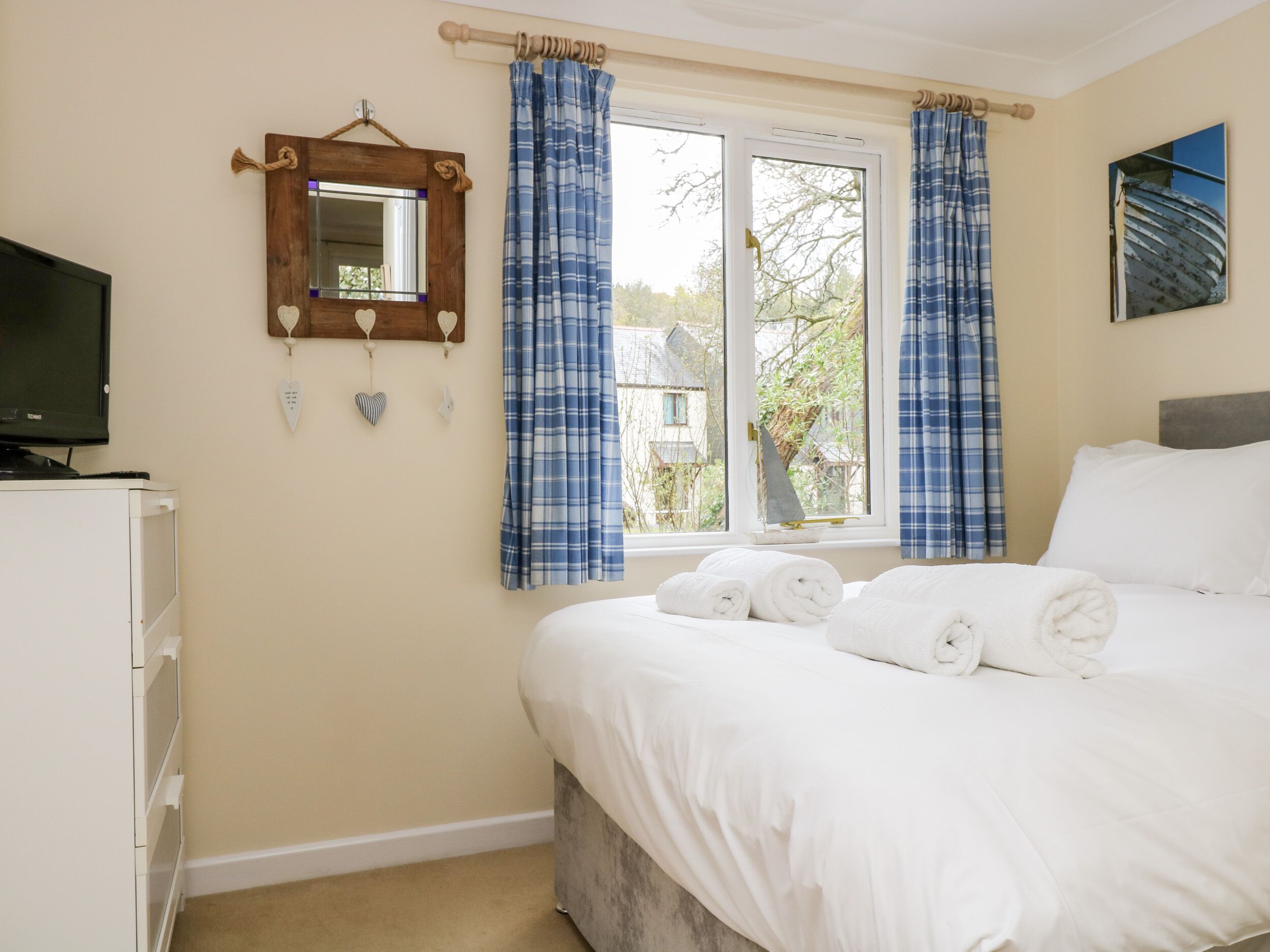 A bedroom with a bed, a television, a dresser, a window with curtains, and a mirror on the wall.