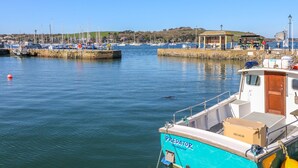 A marina with boats docked, a small building with a roof, and a clear blue sky. - Pugwash Cottage (Falmouth)