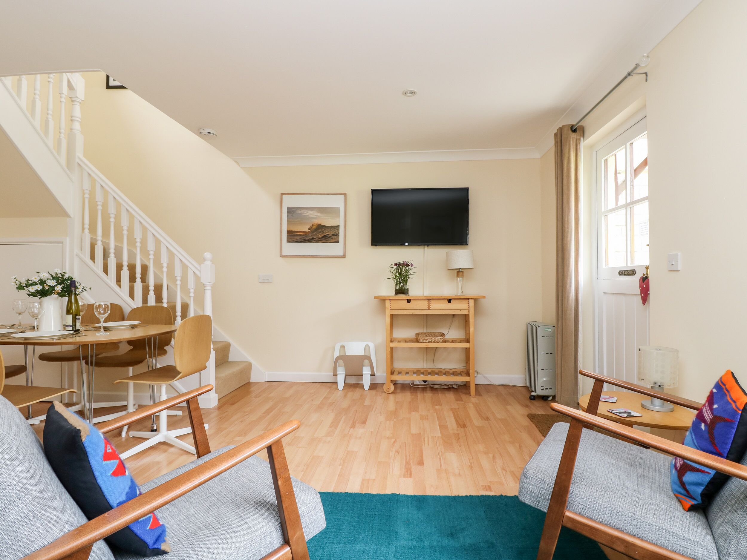 A living room with a staircase, a dining area, a television, and a door with a window.