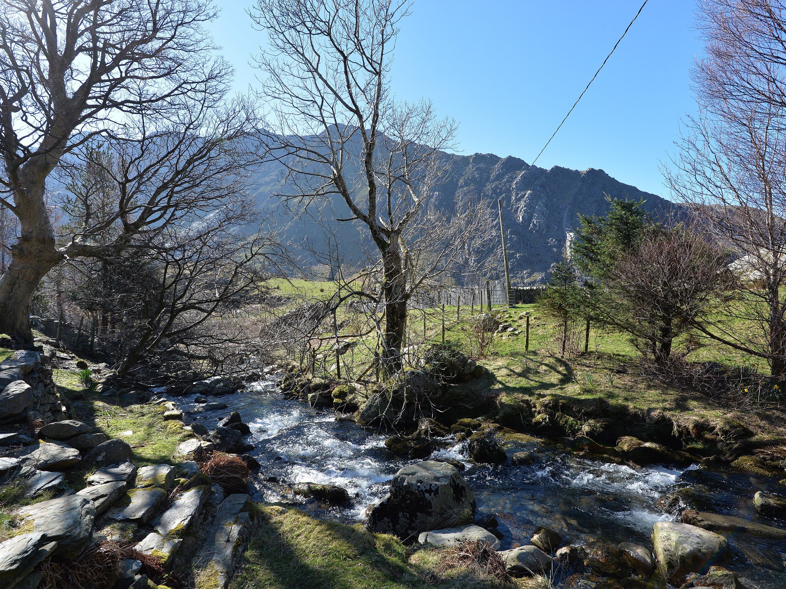 Een natuurlandschap met een beek, rotsachtig terrein en bergen op de achtergrond.