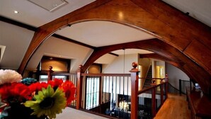 Un intérieur spacieux avec un haut plafond en bois, un escalier et une vue sur l’intérieur grâce à une rambarde en verre.