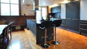 Une cuisine moderne avec des meubles de couleur sombre, un îlot central doté de tabourets de bar et un coin repas avec un plancher en bois et une table.