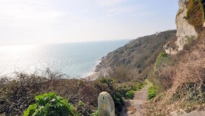 Un sentier côtier, balisé par un repère en pierre, qui mène à une falaise surplombant la mer.