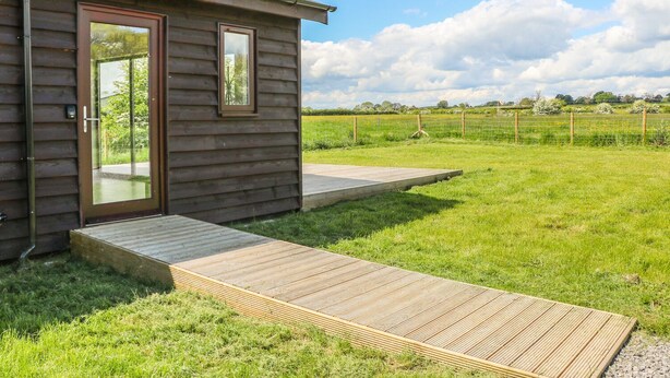A wooden cabin with a glass door, a small deck, and a grassy yard. - Rose Lodge (York)