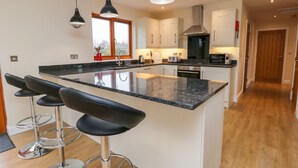 A modern kitchen with a central island, bar stools, pendant lighting, and a view of the outdoors through a window. - Rose Lodge (York)