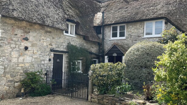 A stone cottage with thatched roofs, a gravel driveway, and a metal gate. - Ivy Cottage (Wareham)