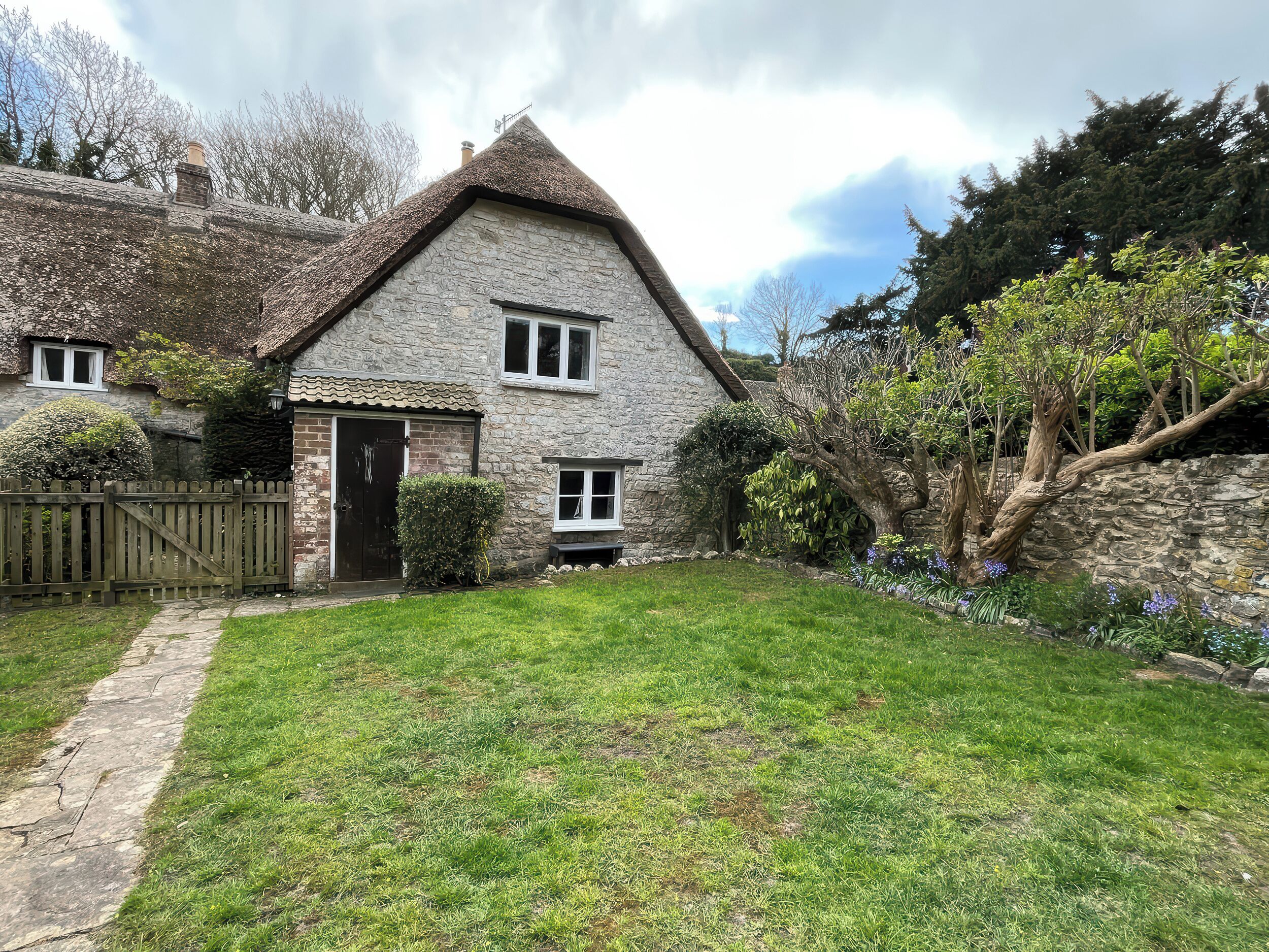 A stone house with a thatched roof, a wooden gate, and a well-maintained lawn.