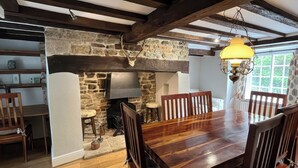 A rustic interior with a stone fireplace, wooden beams, a dining table, and chairs. - Ivy Cottage (Wareham)