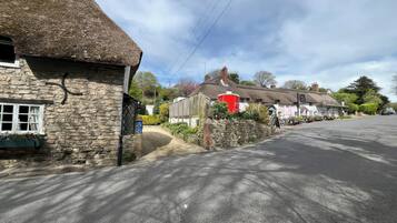 A quaint village street with thatched-roof cottages, a stone wall, and a red building with a sign.